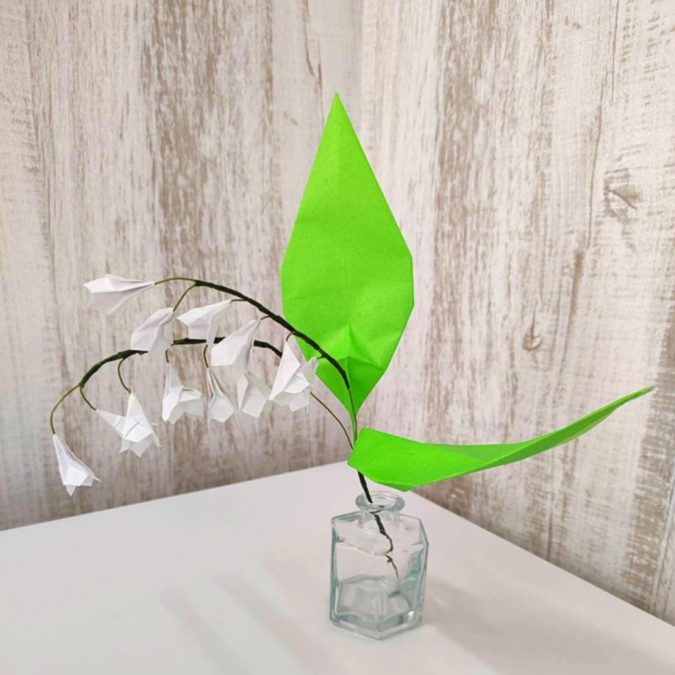 折り紙でできた白いすずらんの花。ガラス瓶に生けられている。